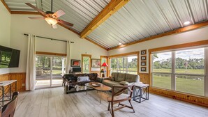 A spacious living room with a ceiling fan, large windows, and a view of the outdoors. - Fish On-site! 35-acre Escape Near Cedar Creek Lake (Malakoff)