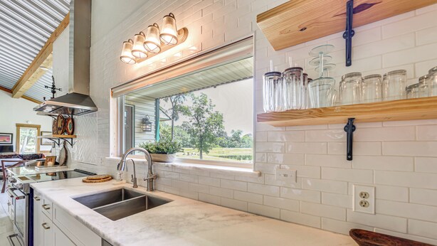 A kitchen with a large window, white tiled backsplash, stainless steel sink, and wooden shelves with jars. - Fish On-site! 35-acre Escape Near Cedar Creek Lake (Malakoff)