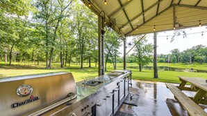 An outdoor grill area with a Char-Broil brand grill, a picnic table, and a covered space with trees in the background. - Fish On-site! 35-acre Escape Near Cedar Creek Lake (Malakoff)
