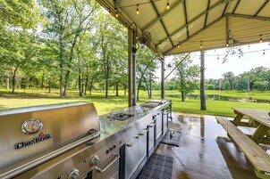 An outdoor grill area with a Char-Broil brand grill, a picnic table, and a covered space with trees in the background.