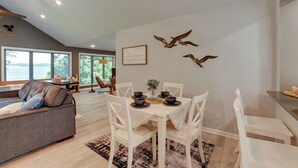 Een moderne woonkamer met een bank, eettafel en stoelen, een groot raam en decoratieve wandkunst.