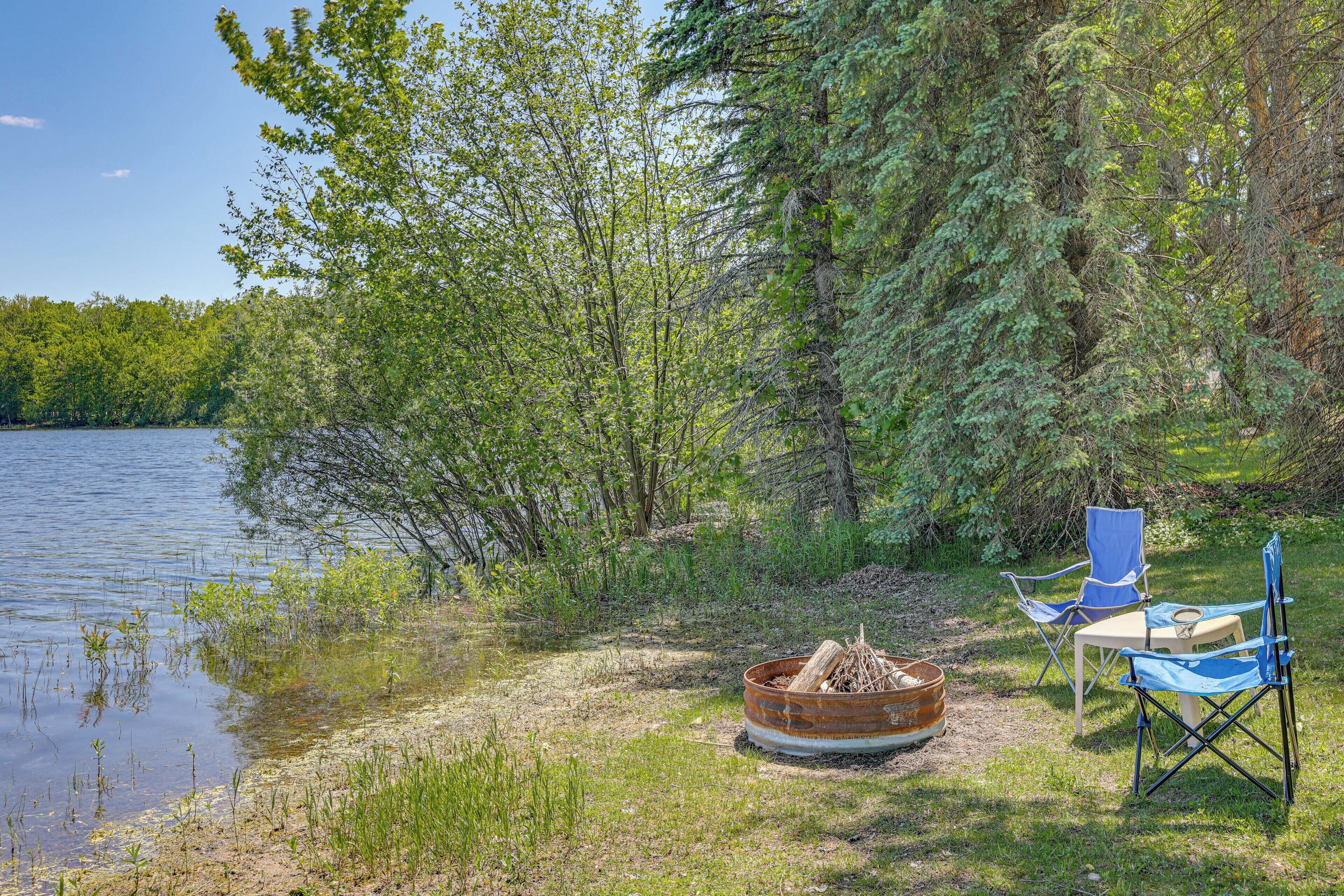 Un espace de camping au bord du lac, équipé d’un foyer, de deux chaises de camping bleues et d’une table.
