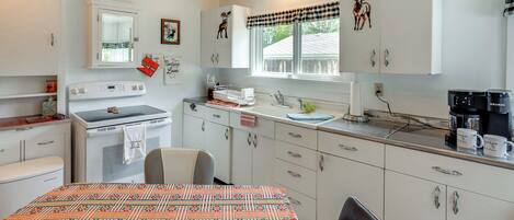 A kitchen with white cabinets, a stove, a refrigerator, a window with a checkered valance, and a wall-mounted deer decoration.