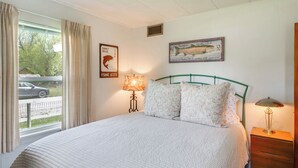 A bedroom with a large bed, a lamp, a dresser, and a window with curtains.