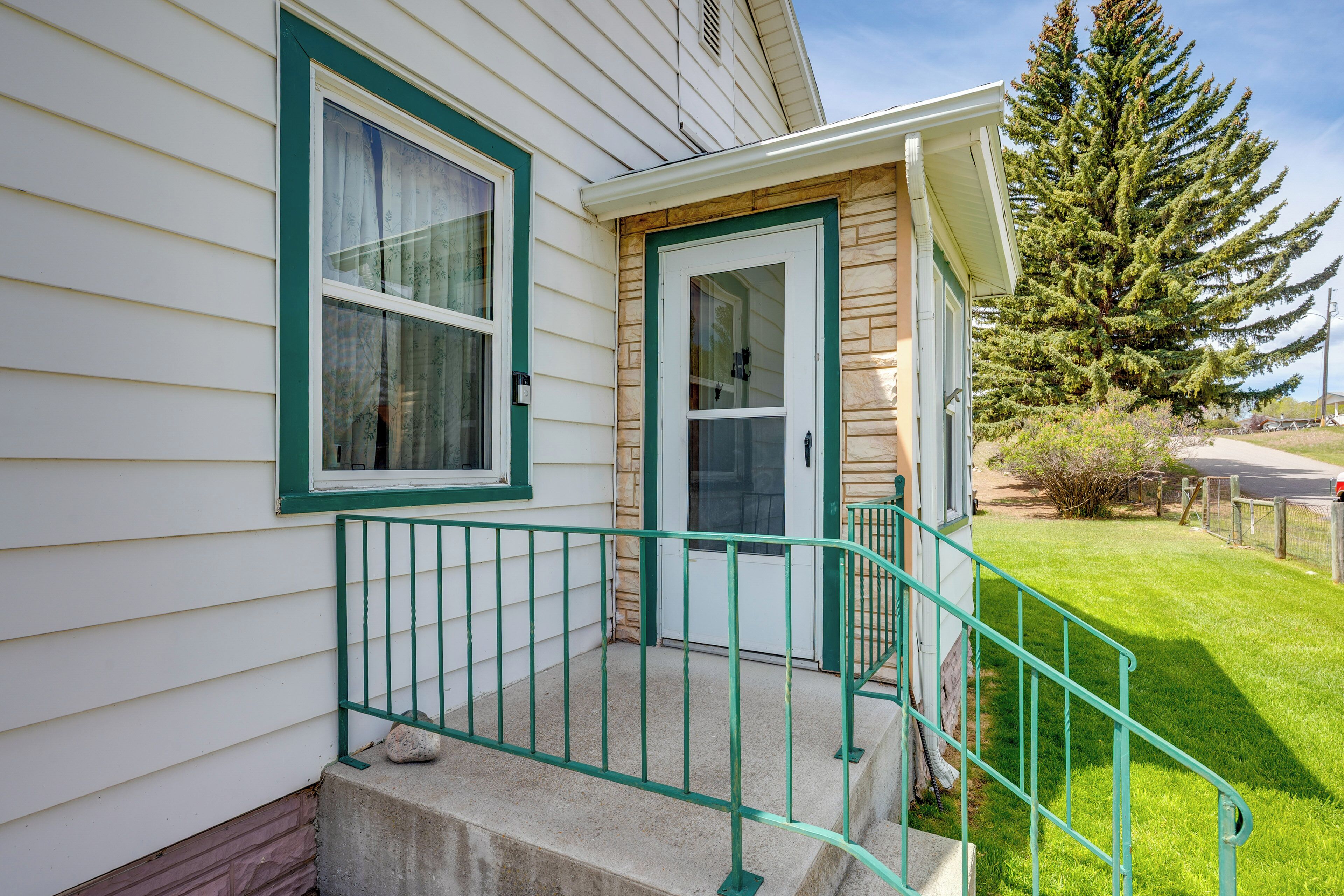 A house with a green front door, a small porch with a green railing, and a large evergreen tree in the background.