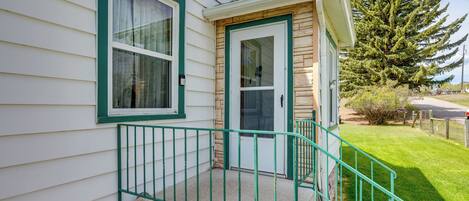A house with a green front door, a small porch with a green railing, and a large evergreen tree in the background.