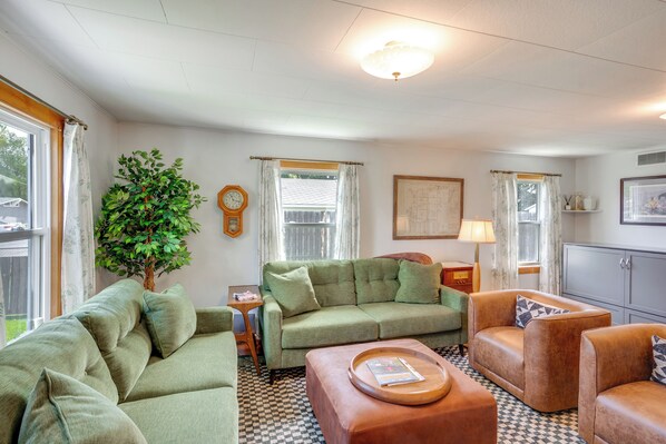 A living room with a green sofa, a brown armchair, a wooden coffee table, and a large green plant.