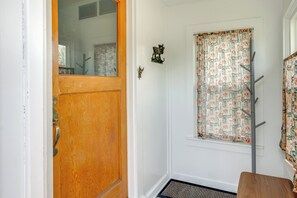 Eine Holztür, ein Fenster mit gemusterten Vorhängen, ein Kleiderständer und ein kleiner Holztisch.