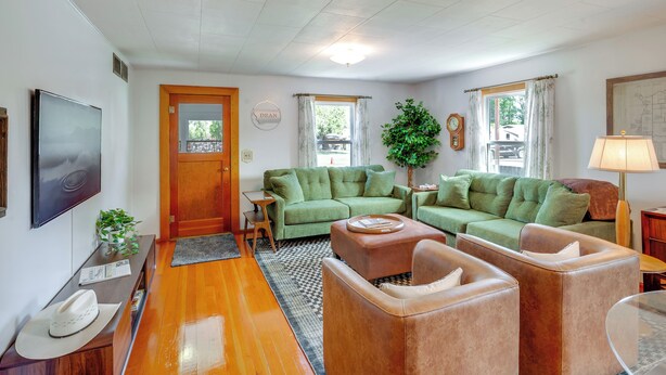 A living room with a green sofa, a brown leather armchair, a coffee table, and a television on the wall.