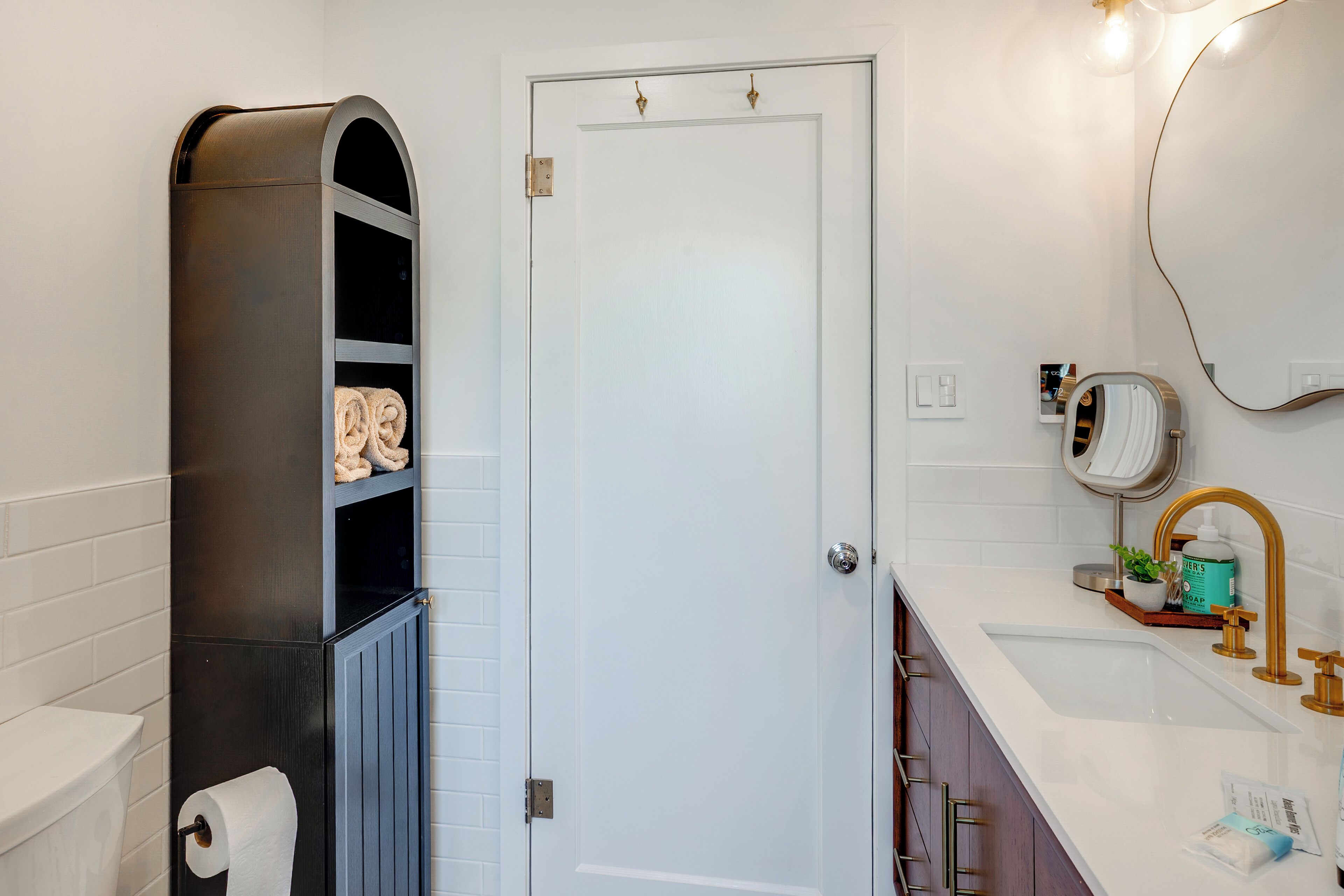 A bathroom with a toilet, a towel rack, a sink with a mirror, and a towel shelf.