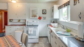 A kitchen with white cabinets, a stove, a sink, and a window with a view.
