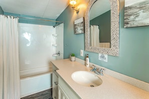 A bathroom with a sink, mirror, shower, and towel rack.