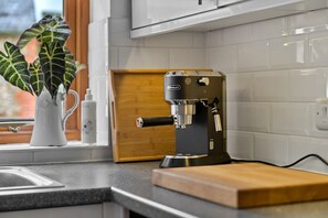 A kitchen with a coffee machine, a wooden cutting board, and a window with a plant. - Poundtree (Wherwell)