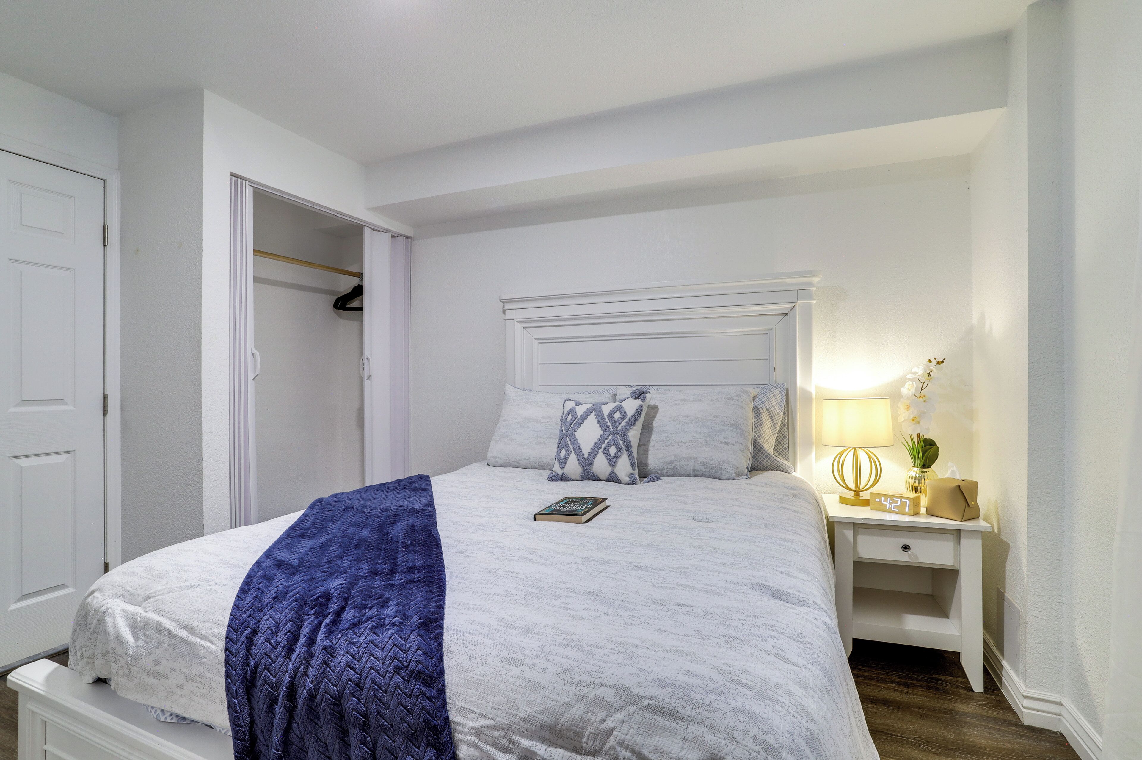 Une chambre bien rangée, avec un lit, une table de chevet, une lampe et une armoire.