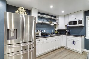 Una cocina moderna con refrigerador de acero inoxidable, armarios blancos y microondas.