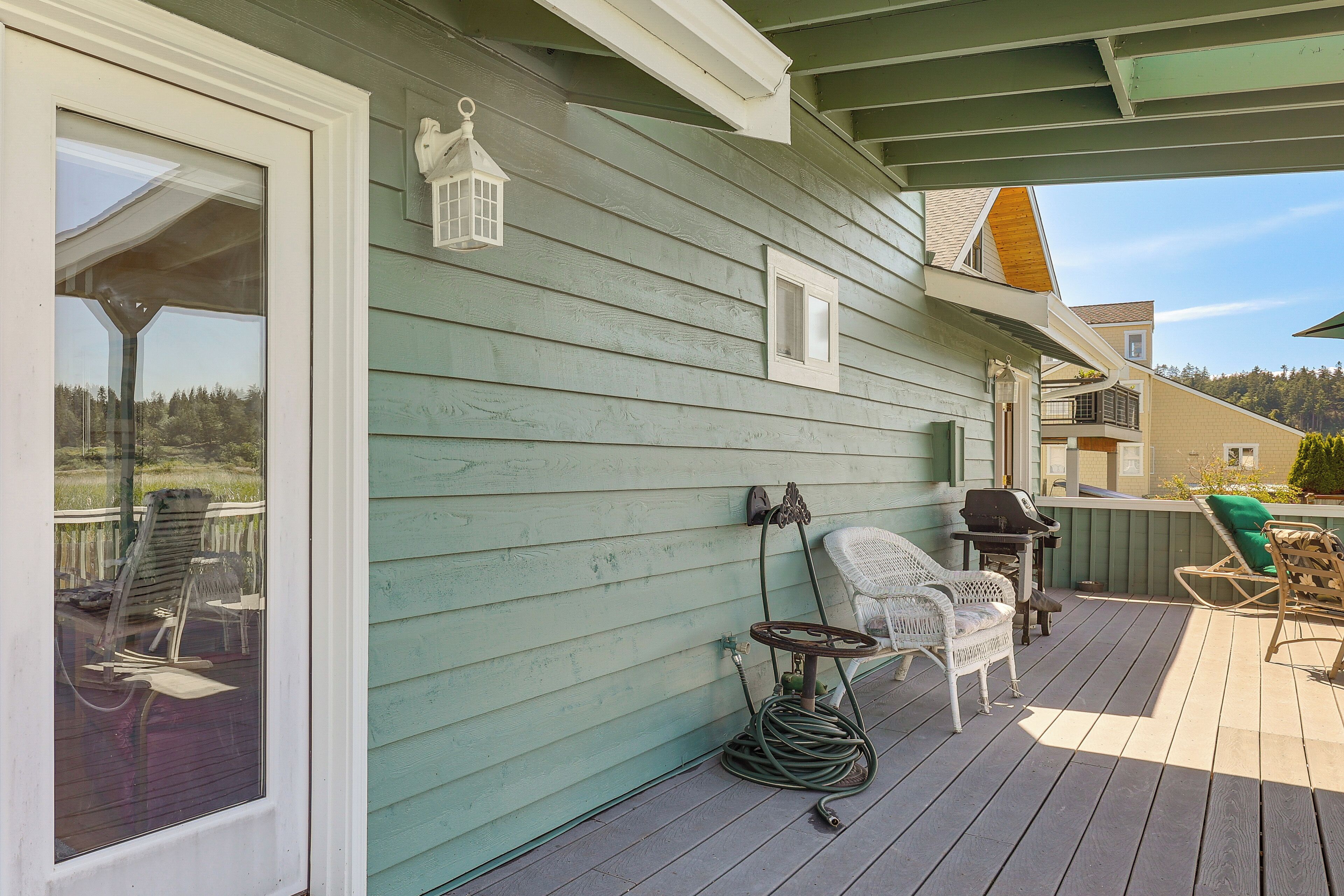 Une terrasse couverte, aménagée avec du mobilier d’extérieur, une lanterne et un tuyau d’arrosage.