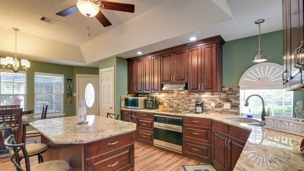 A kitchen with wooden cabinets, a granite countertop, a ceiling fan, and a built-in microwave. - Pool & Covered Patio! Galveston County Getaway (Dickinson)