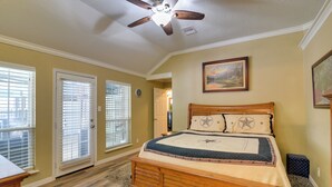 A bedroom with a wooden bed, a ceiling fan, and a painting on the wall. - Pool & Covered Patio! Galveston County Getaway (Dickinson)