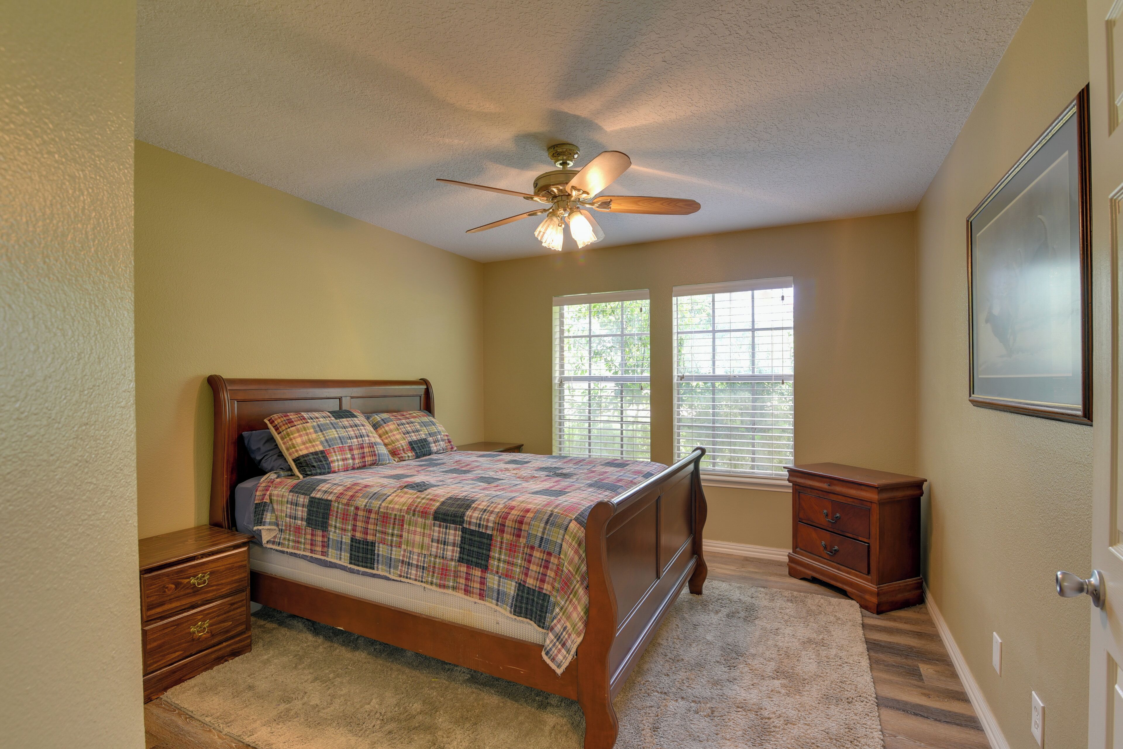 A bedroom with a bed, a nightstand, a dresser, a ceiling fan, and a window.