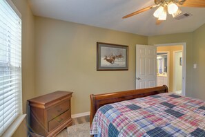 Ein Schlafzimmer mit Bett, Kommode, Deckenventilator und einer Tür zu einem anderen Raum.