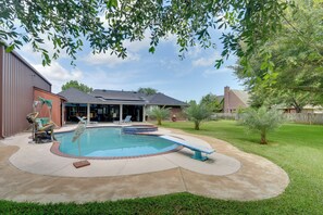 Un patio trasero con piscina, un porche cubierto y un jardín cercado.