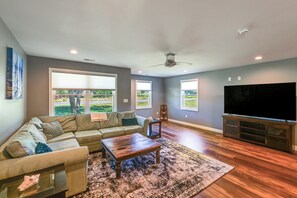 A living room with a sectional sofa, a coffee table, a TV stand, and large windows.