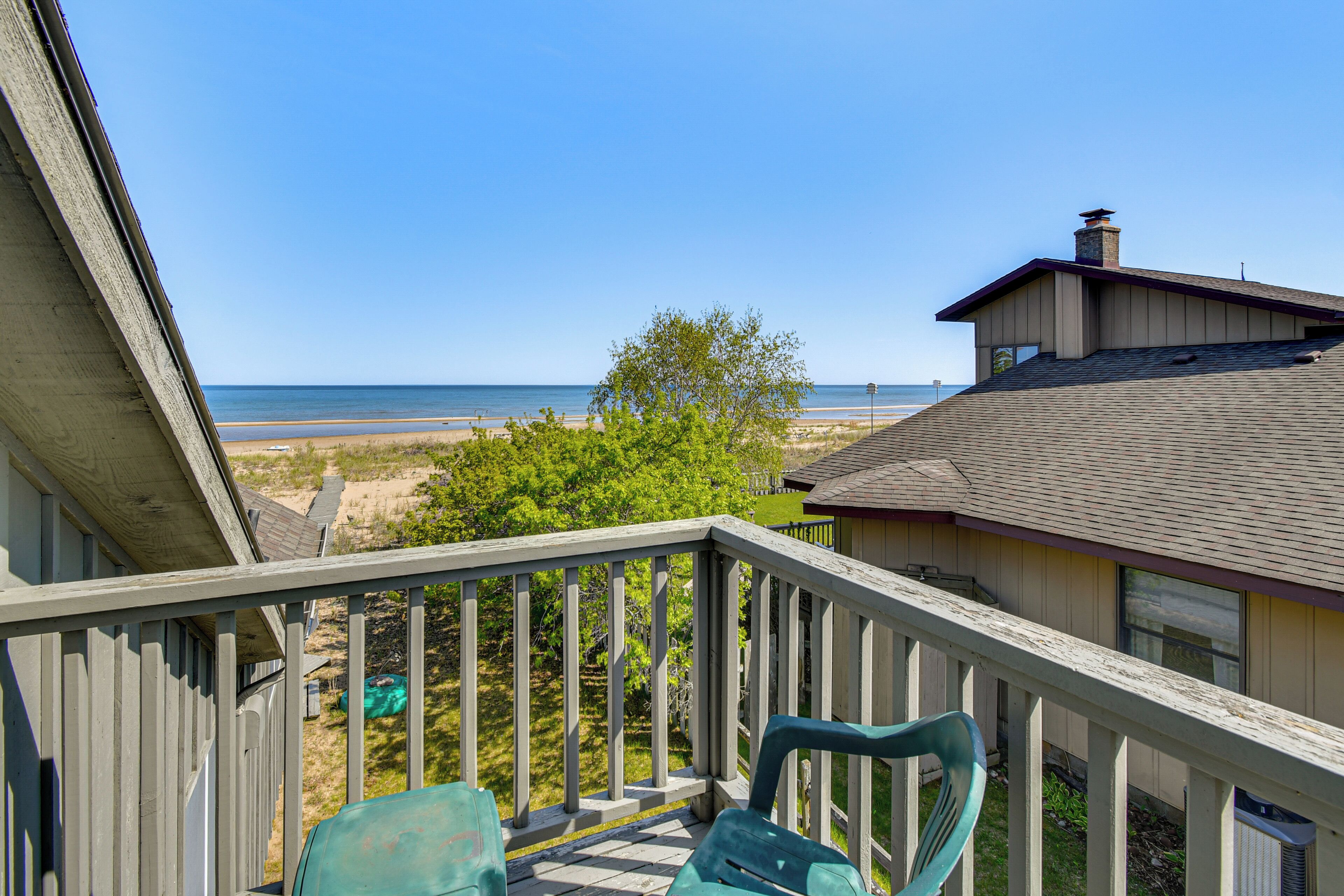 A balcony with a view of the beach, a wooden railing, and a chair.