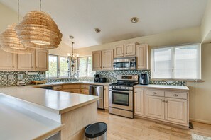 A kitchen with a large island, stainless steel appliances, wooden cabinets, and a tiled backsplash.