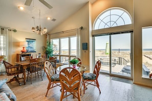 A spacious living area with a dining table, chairs, and a view of the beach through large windows.
