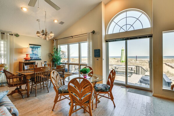A spacious living area with a dining table, chairs, and a view of the beach through large windows.