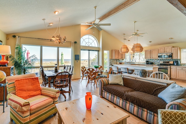 A spacious living area with a sofa, chairs, a dining table, and a kitchen with cabinets and appliances.