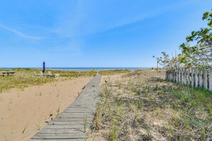 A wooden boardwalk leading to a beach with a picnic table and chairs, and a fence on the right.
