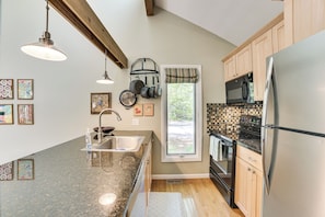 A modern kitchen with granite countertops, stainless steel appliances, wooden cabinets, and a window with a view.