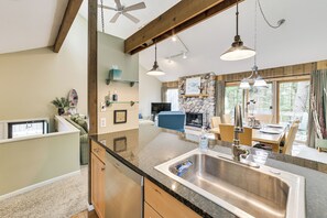 A kitchen with a granite countertop, stainless steel sink, wooden cabinets, and pendant lighting. - Harbor Springs Condo: Walk to Beach & Pools! (Harbor Springs)