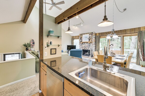 A kitchen with a granite countertop, stainless steel sink, wooden cabinets, and pendant lighting.