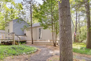 A cabin with a deck, surrounded by trees and a gravel path. - Only 8/22-8/29 Still Available for Summer 2026! (Harbor Springs)