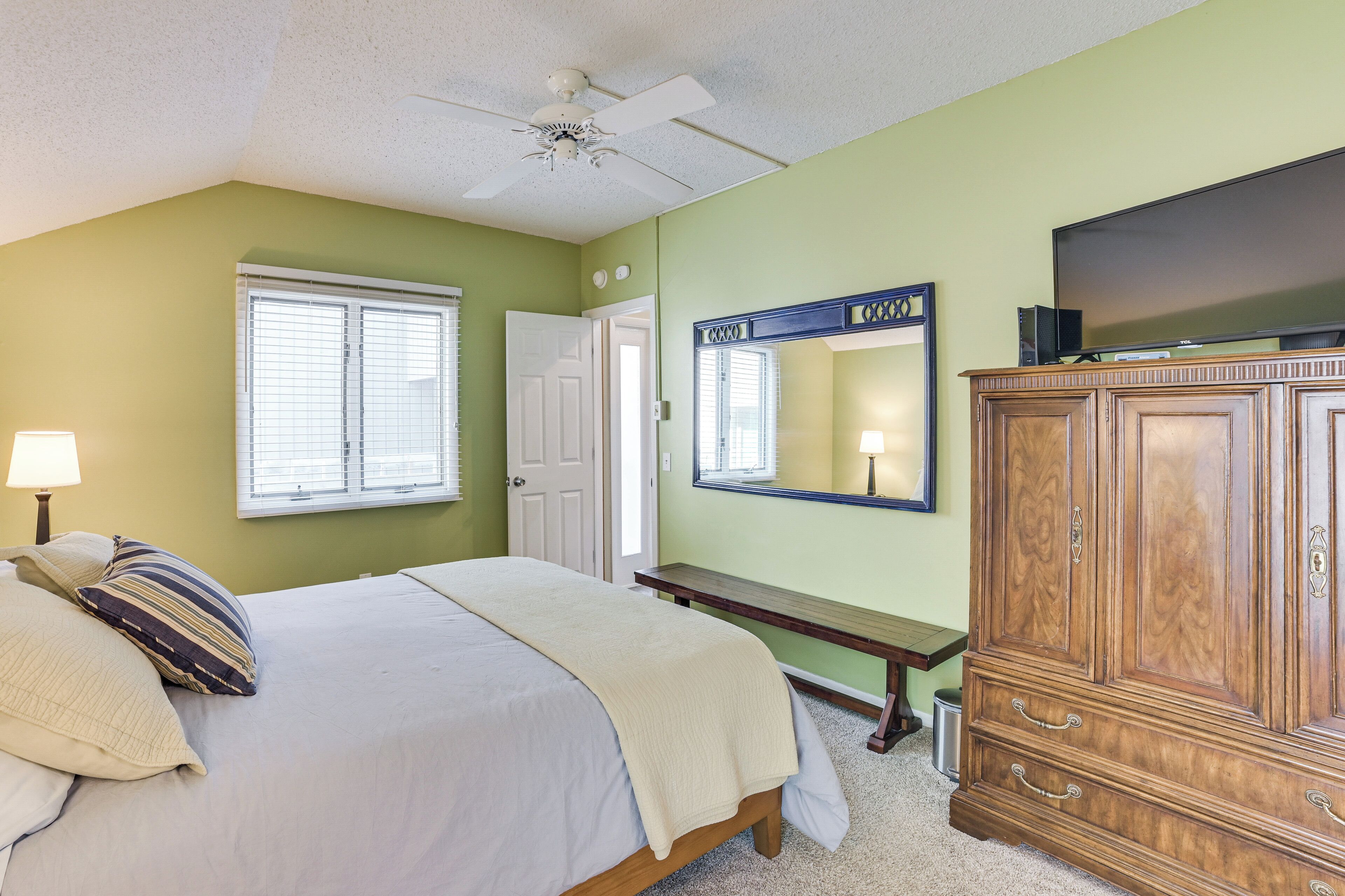 A bedroom with a bed, a nightstand, a dresser, a television, and a ceiling fan.