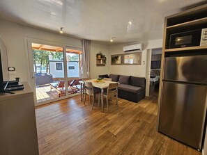 A modern kitchen with a stainless steel refrigerator, a dining area with a table and chairs, and a sliding glass door leading to an outdoor patio. - Mobile home LAMA 1076 - Luxury & peace at Soline Camping Park (Biograd na Moru)