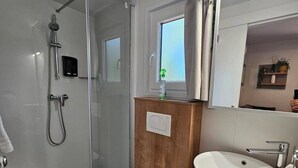 Uma casa de banho moderna com cabine de duche em vidro, sanita, lavatório e janela.