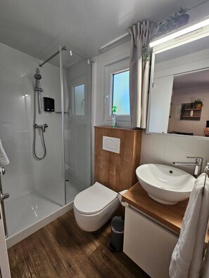 A modern bathroom with a glass shower enclosure, a toilet, a sink, and a window. - Mobile home LAMA 1076 - Luxury & peace at Soline Camping Park (Biograd na Moru)