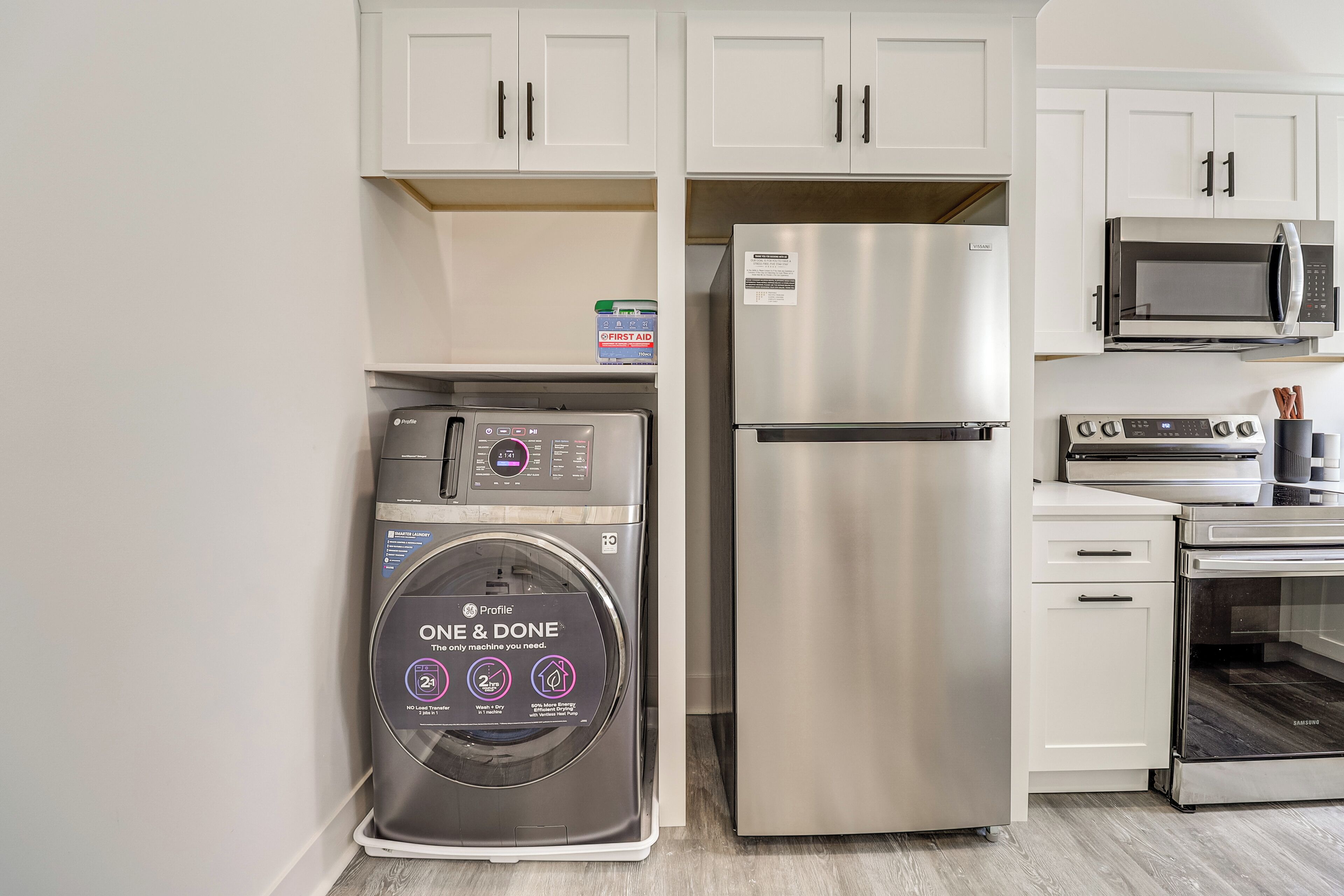 A compact kitchen with a stainless steel refrigerator, a washing machine, and a microwave.