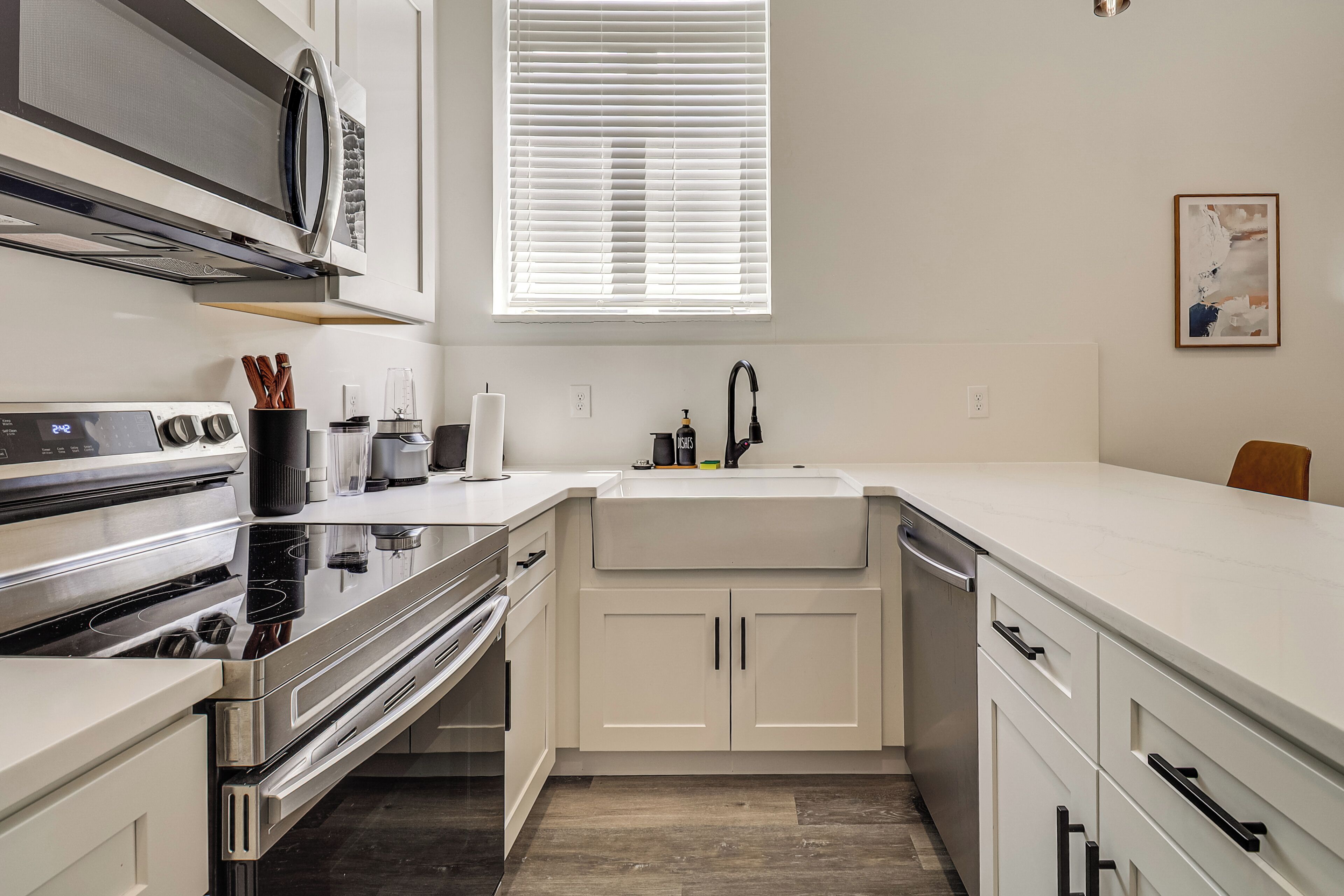 A modern kitchen with white cabinetry, a stainless steel stove, and a window with blinds.