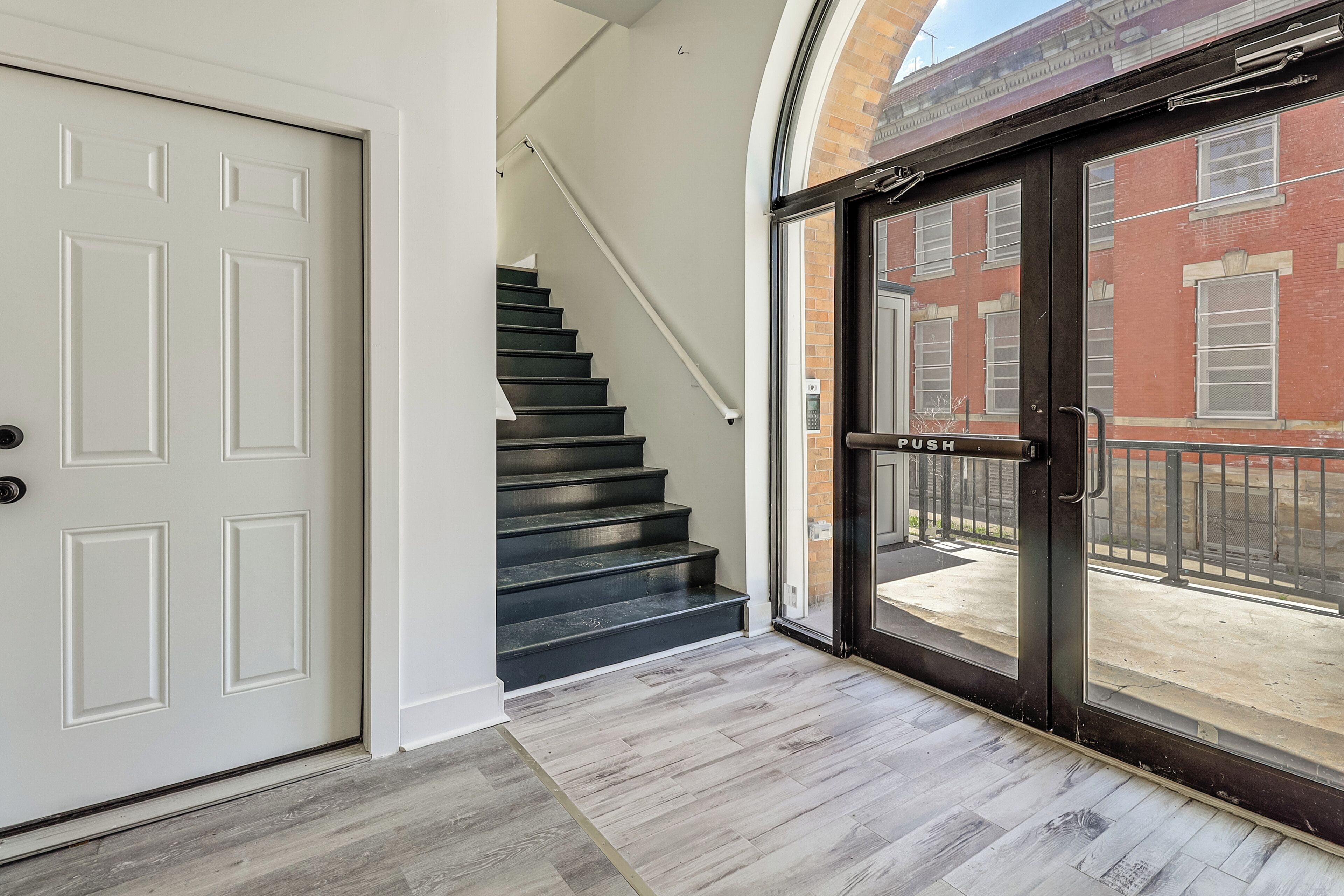 Un escalier menant à un palier du deuxième étage, avec une porte et une entrée vitrée.