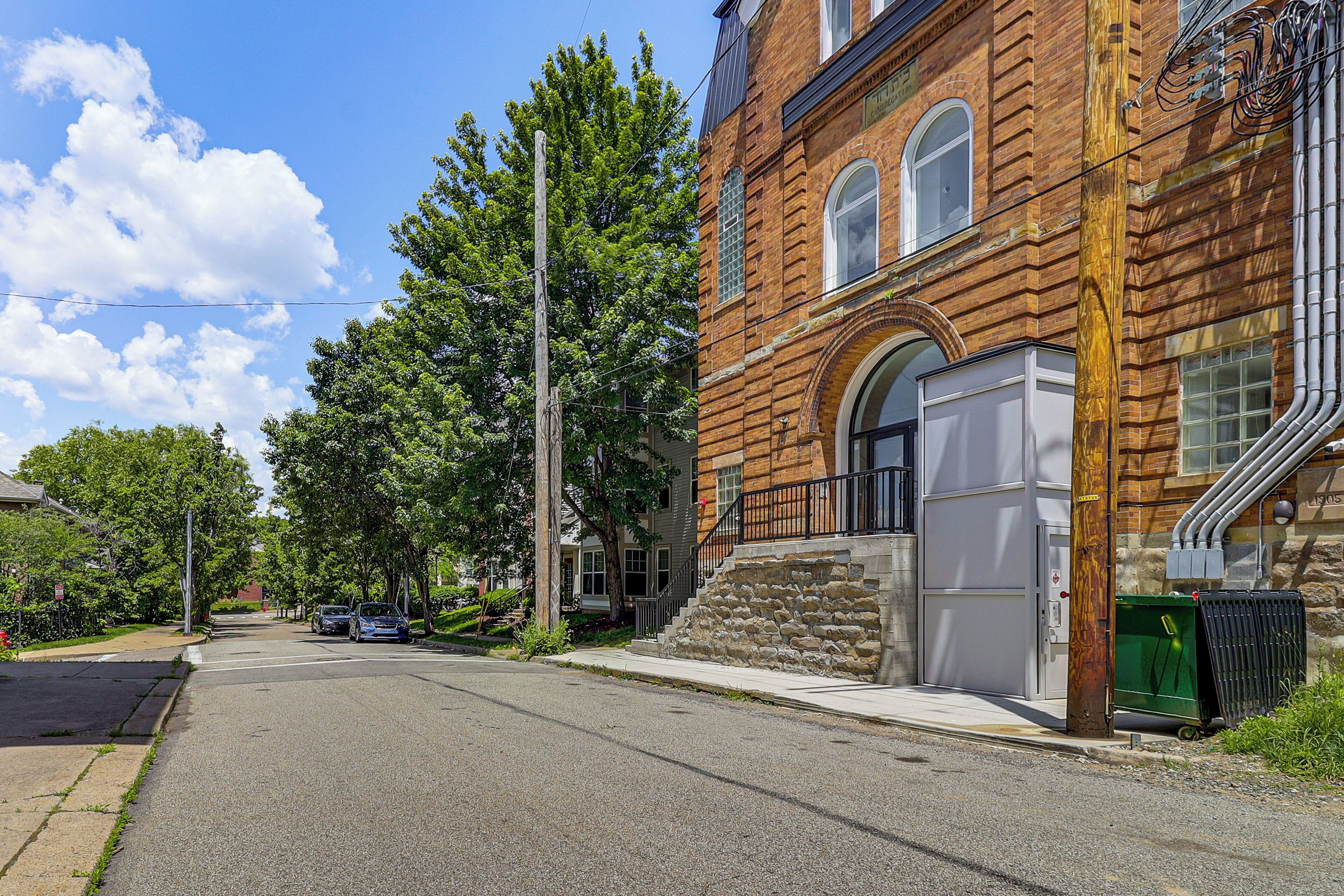 A street view with a brick building, a sidewalk, and parked cars.