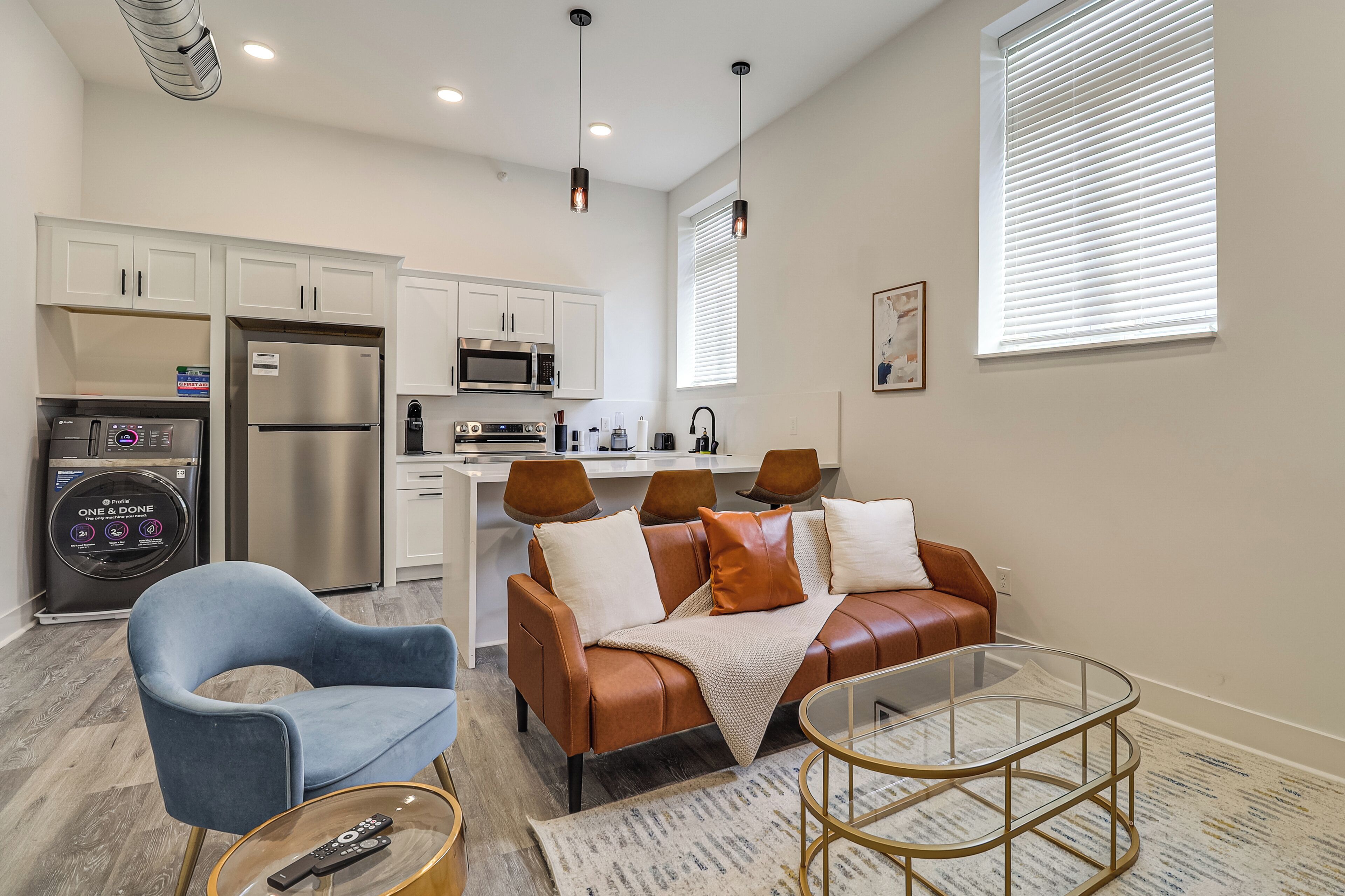 A compact living space with a kitchenette, a sofa, a chair, and a glass coffee table.