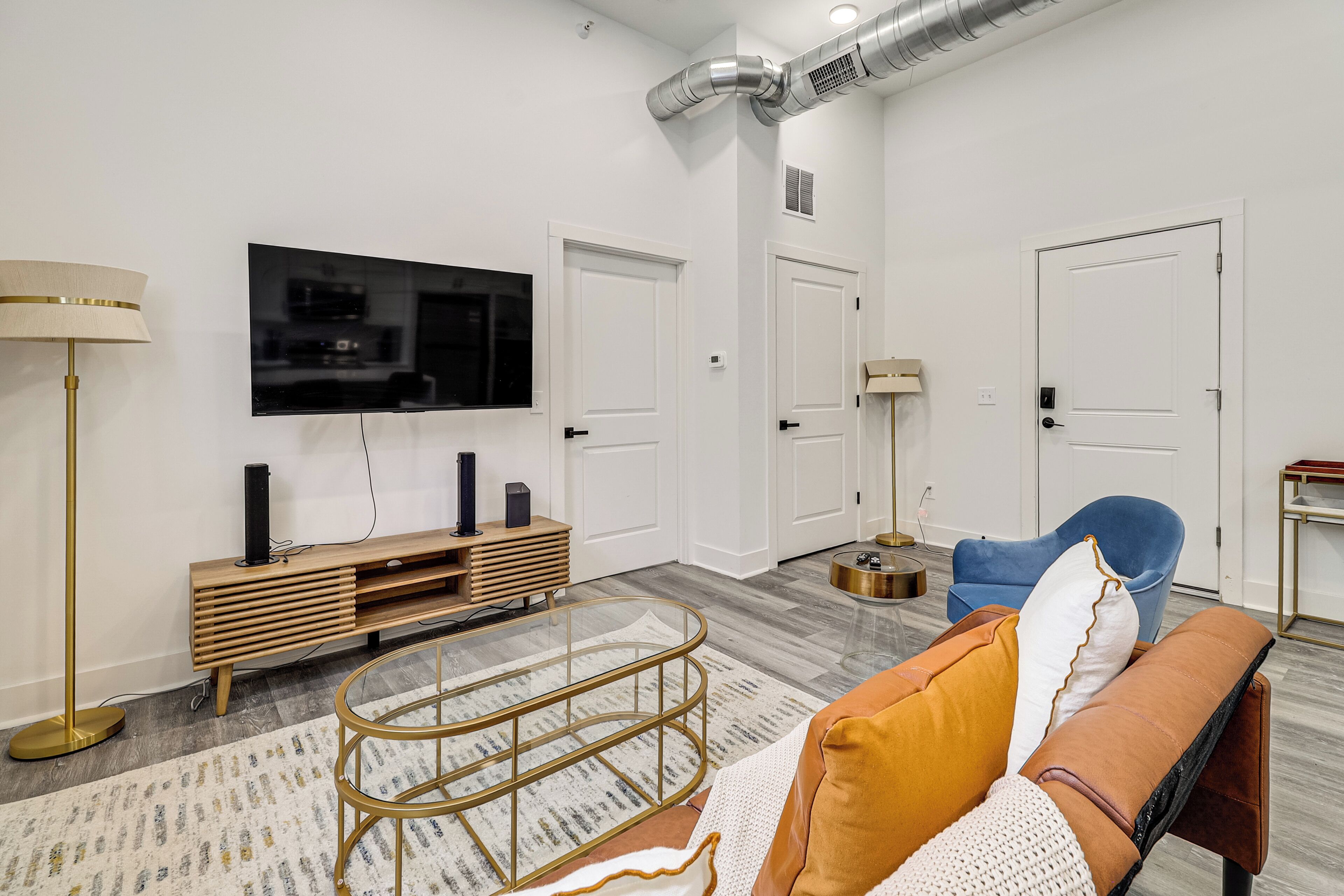Uma sala de estar moderna com televisão de tela plana, um rack de madeira, uma mesa de centro redonda, uma poltrona azul e um sofá marrom.