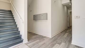 Eine Treppe führt zu einem Flur mit Holzboden, einem an der Wand montierten Stromverteiler und einer Tür am Ende.