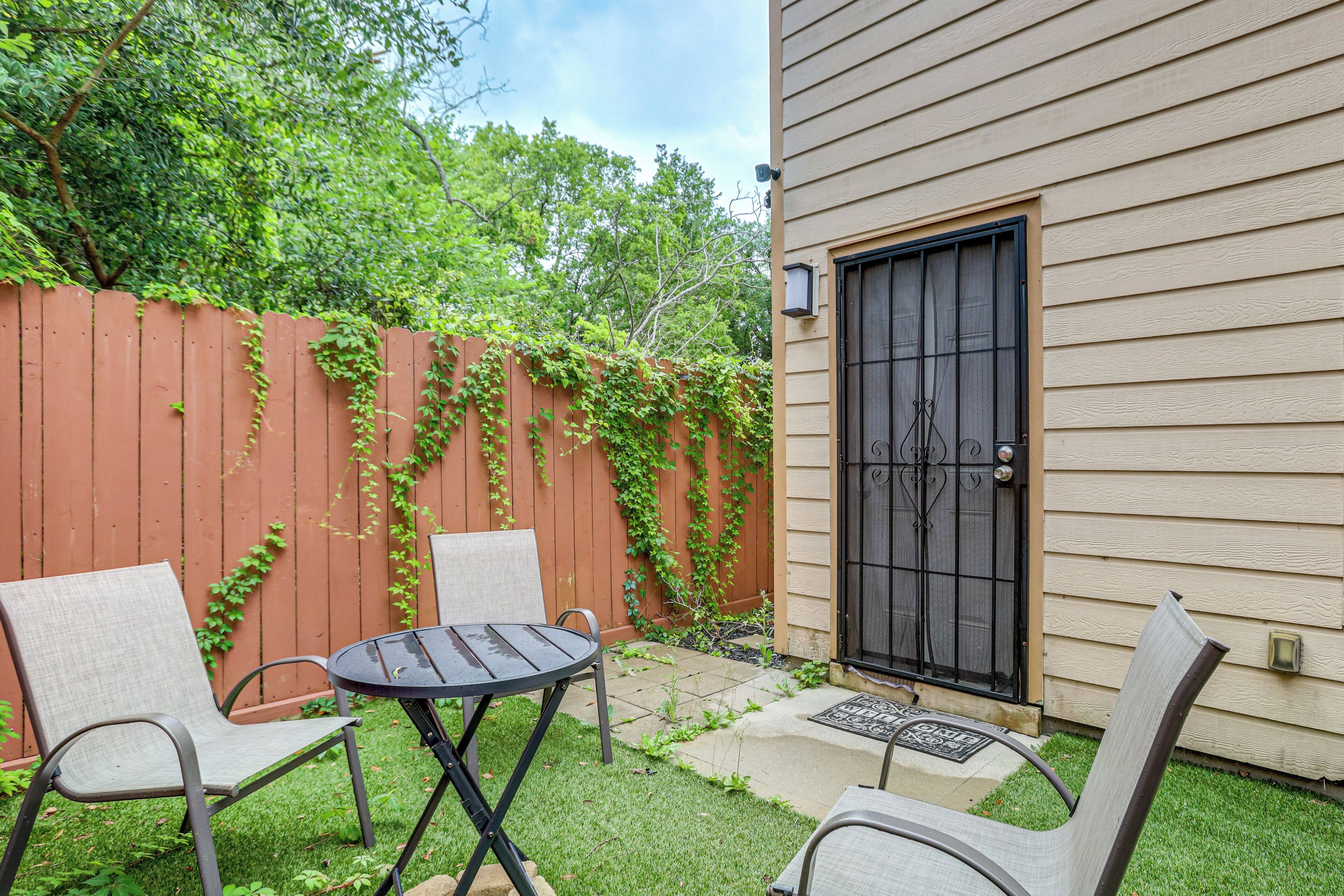 A patio with two chairs and a table, a wooden fence, and a house with a black door.
