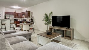 Een woonkamer met een bank, een televisie en een keuken op de achtergrond.