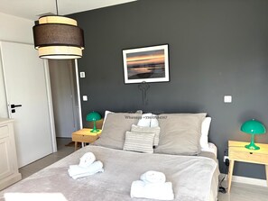 Un dormitorio con una cama, dos mesitas de noche, una lámpara colgante, un cuadro enmarcado en la pared y una puerta.